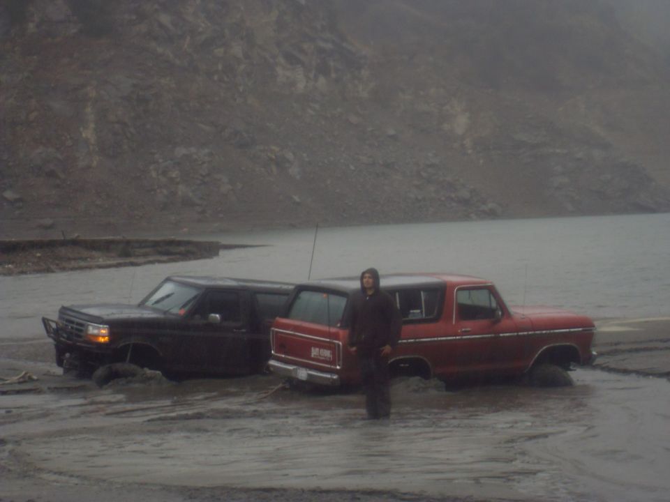 Red 1979 Ford Bronco and black SUV stuck in mud