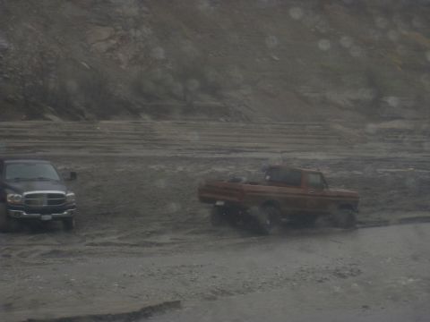 1979 Ford Bronco - Two trucks navigate a muddy terrain, with one appearing to be an older model pickup.