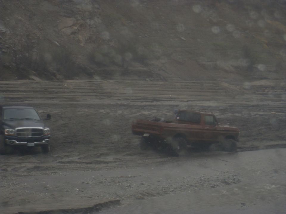 red pickup truck and black pickup truck driving on a muddy road