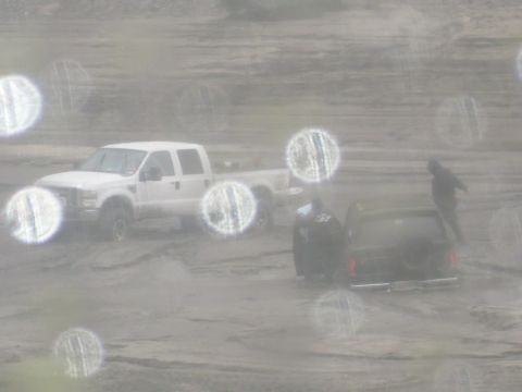 1979 Ford Bronco - A black SUV with a rear-mounted spare tire is stuck in the mud alongside a white pickup truck.