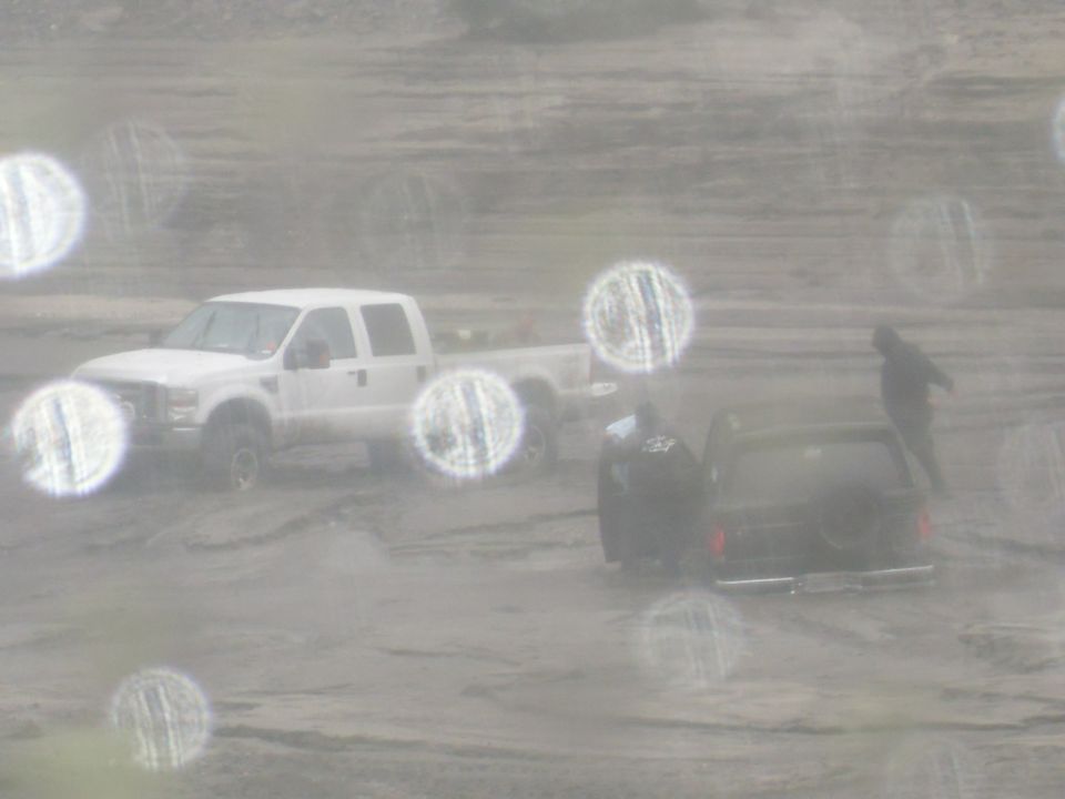 Black SUV with spare tire on rear, in a muddy scene with a white pickup truck