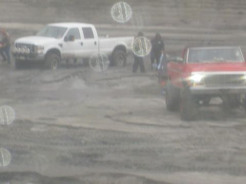 1979 Ford Bronco - Two pickup trucks are stuck in the mud with several people observing the scene.