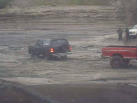 1979 Ford Bronco - A black Ford Bronco is being towed by a red pickup truck across a sandy area.