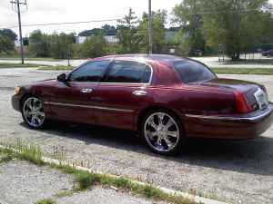 2000 Lincoln Town Car - A red Lincoln Town Car is parked on a paved surface with some grass and trees in the background.