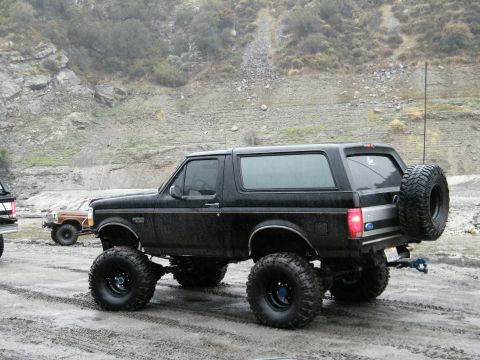 1982 Ford Bronco - This lifted black Ford Bronco, likely a 1992 model, is shown in a three-quarter front view with a spare tire mounted on the rear.