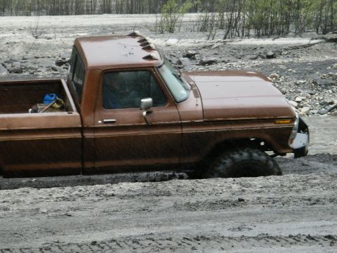 1982 Ford Bronco - A brown pickup truck is stuck in mud, with its front tire submerged.
