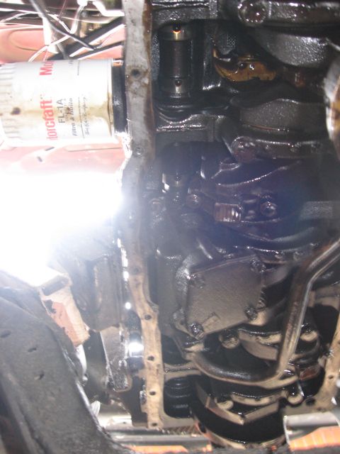 1981 Ford Bronco - Underhood shot down the side of a black, oil-wet engine block showing the oil pan rail, exhaust manifold and steering linkage, taken from b…