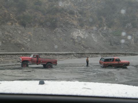1982 Ford Bronco - Two vehicles are stuck in a muddy area near a rocky hillside, with a person observing the situation.
