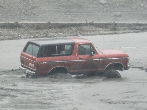 1982 Ford Bronco - This red SUV, likely a 1978 Ford Bronco, is stuck in muddy terrain, with its wheels partially submerged.