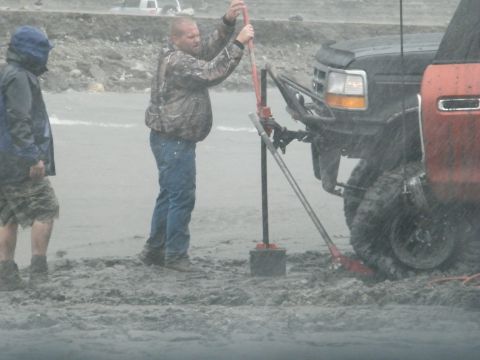 1982 Ford Bronco - Two men attempt to free a stuck black Ford F-Series truck in muddy conditions.