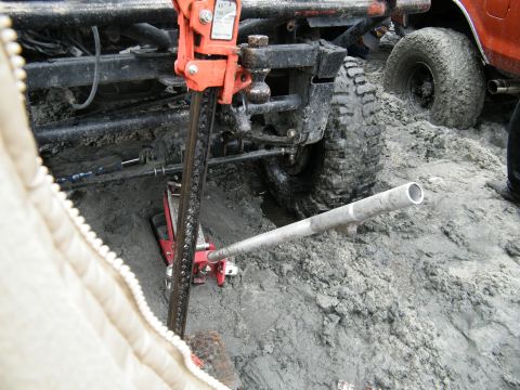 1982 Ford Bronco - A vehicle is stuck in the mud and being lifted by a jack, with another vehicle visible nearby.