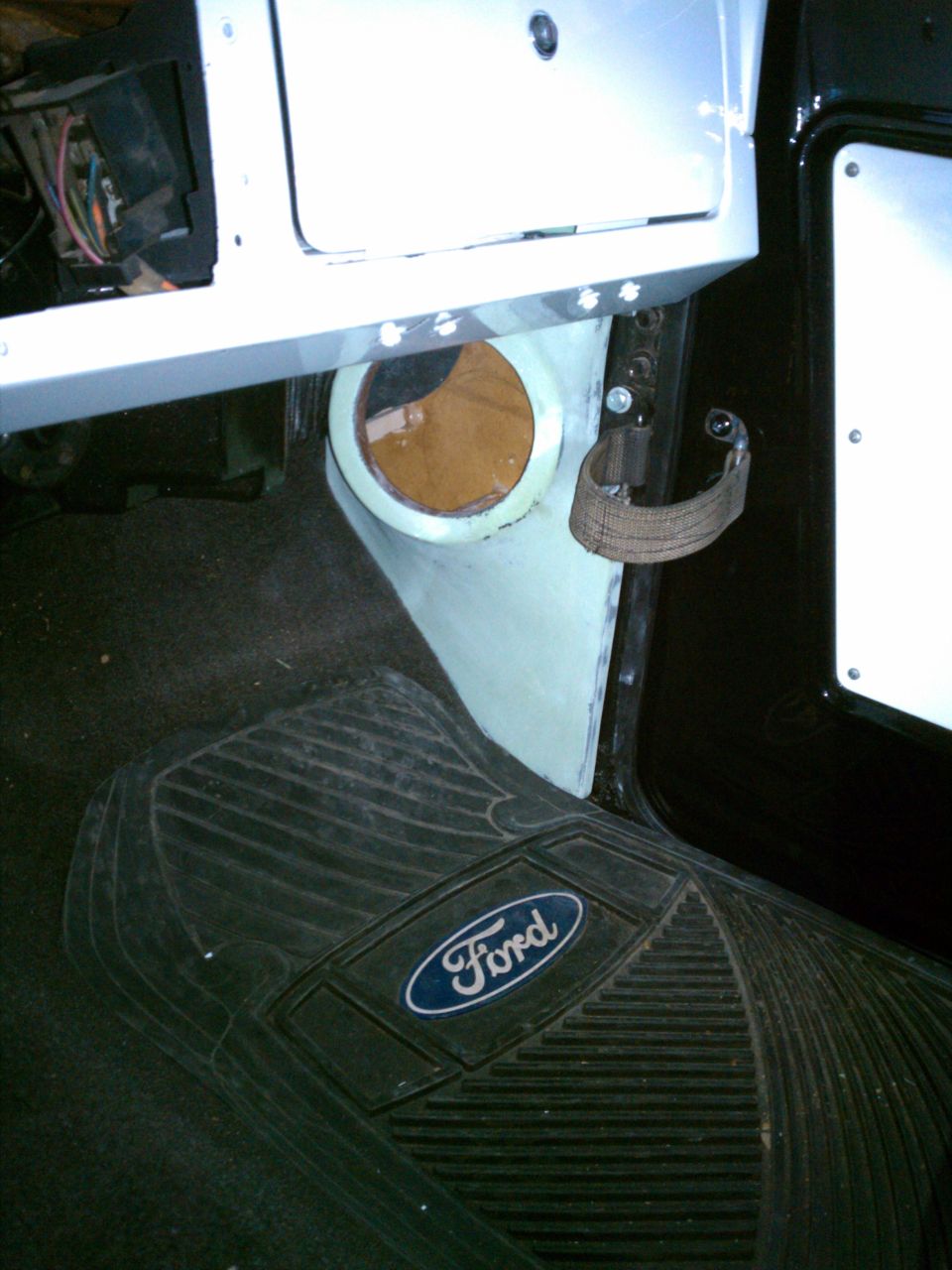 Ford floor mat with oval logo beside custom white panel and exposed wiring in vehicle interior