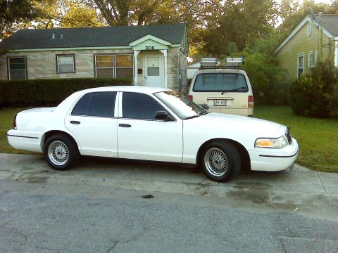 2005 Ford Crown Victoria - A white 2005 Ford Crown Victoria sedan is parked on the street in front of a house.