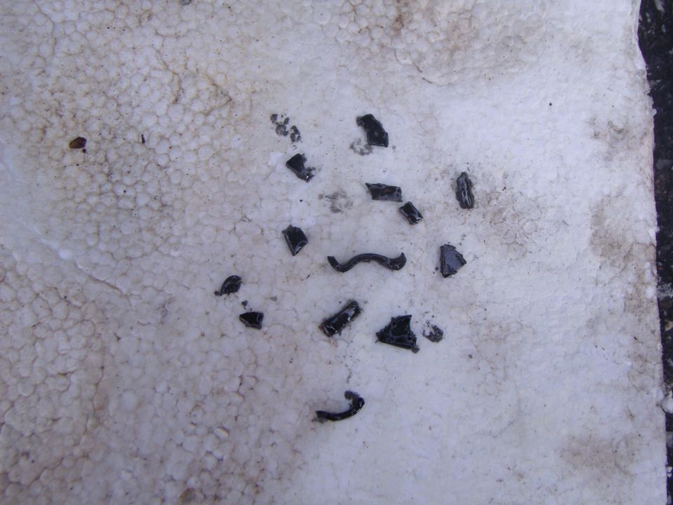 Shards of black plastic and debris scattered on a textured white surface