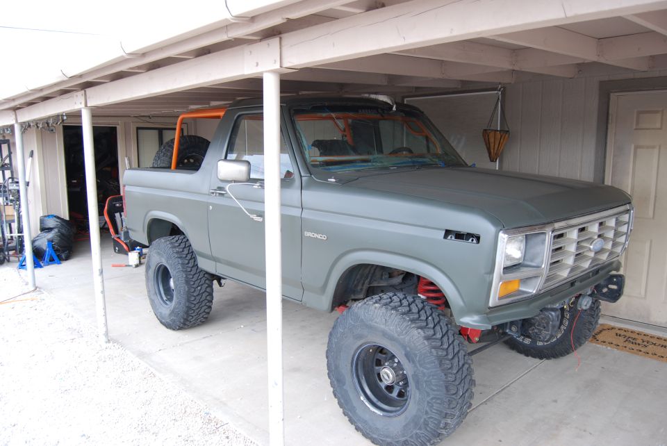 Green Ford Bronco with off-road tires parked under a carport