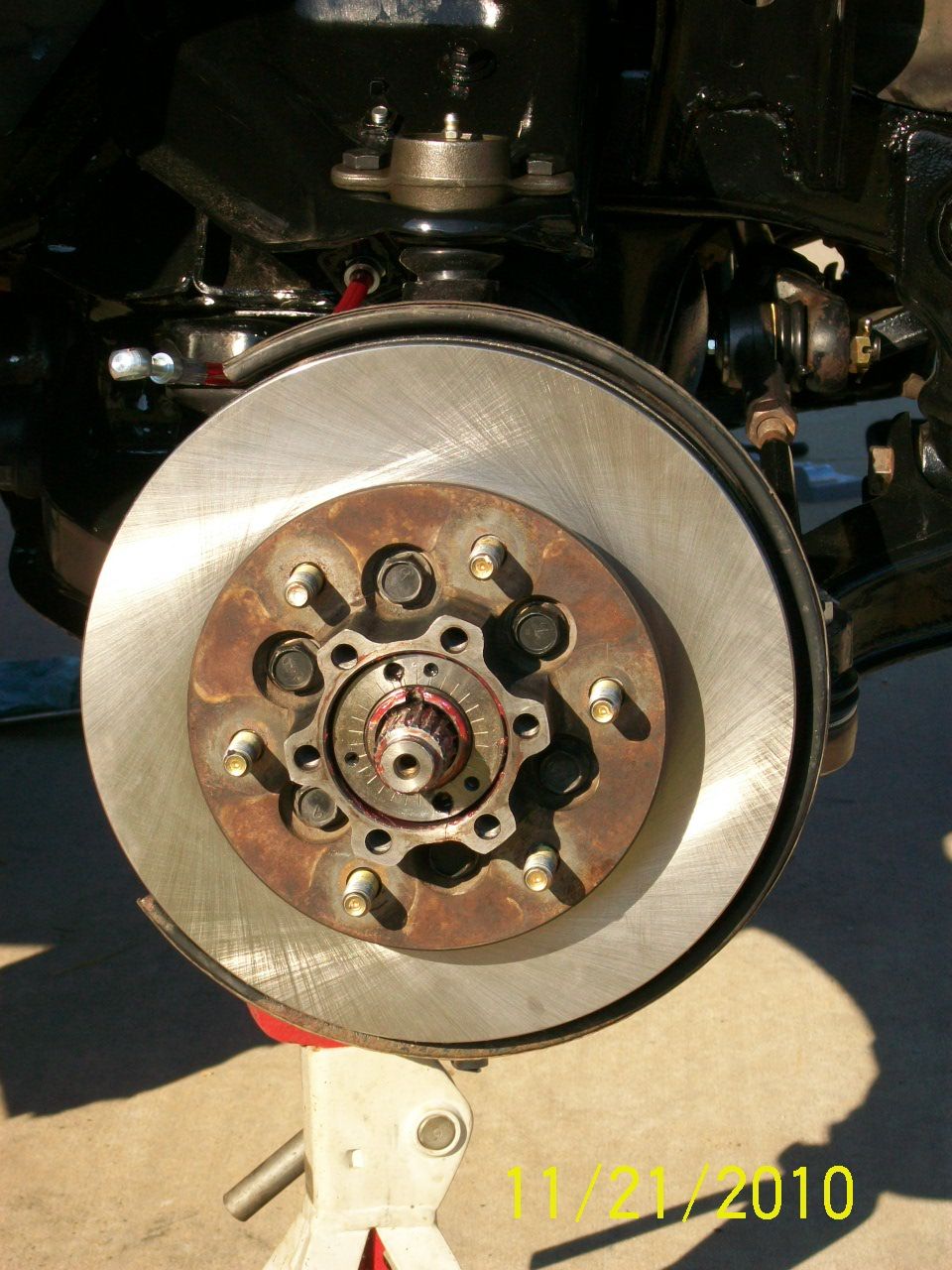 Brake rotor assembly on a jack stand, showing hub, lug nuts, and suspension parts