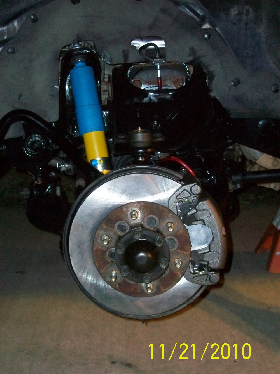Close-up of a vehicle's front suspension with a blue and yellow shock absorber and a brake rotor and caliper