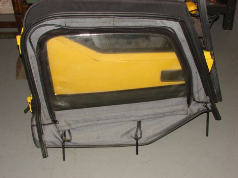 1993 Jeep Wrangler - A yellow Jeep door with its soft top window removed is displayed, revealing the grey fabric and black zippers of the soft top.
