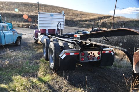 1959 Kenworth W900A - A semi-truck chassis is parked outdoors next to a vintage blue pickup truck and a sports car.