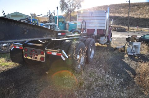 1959 Kenworth W900A - Rear view of a truck chassis with dual rear wheels and chrome mud flaps parked in a lot with other vehicles.