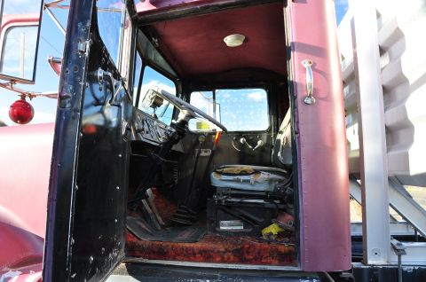 1959 Kenworth W900A - The interior of a vintage truck cab is visible, the driver's seat, steering wheel, and dashboard with worn upholstery.