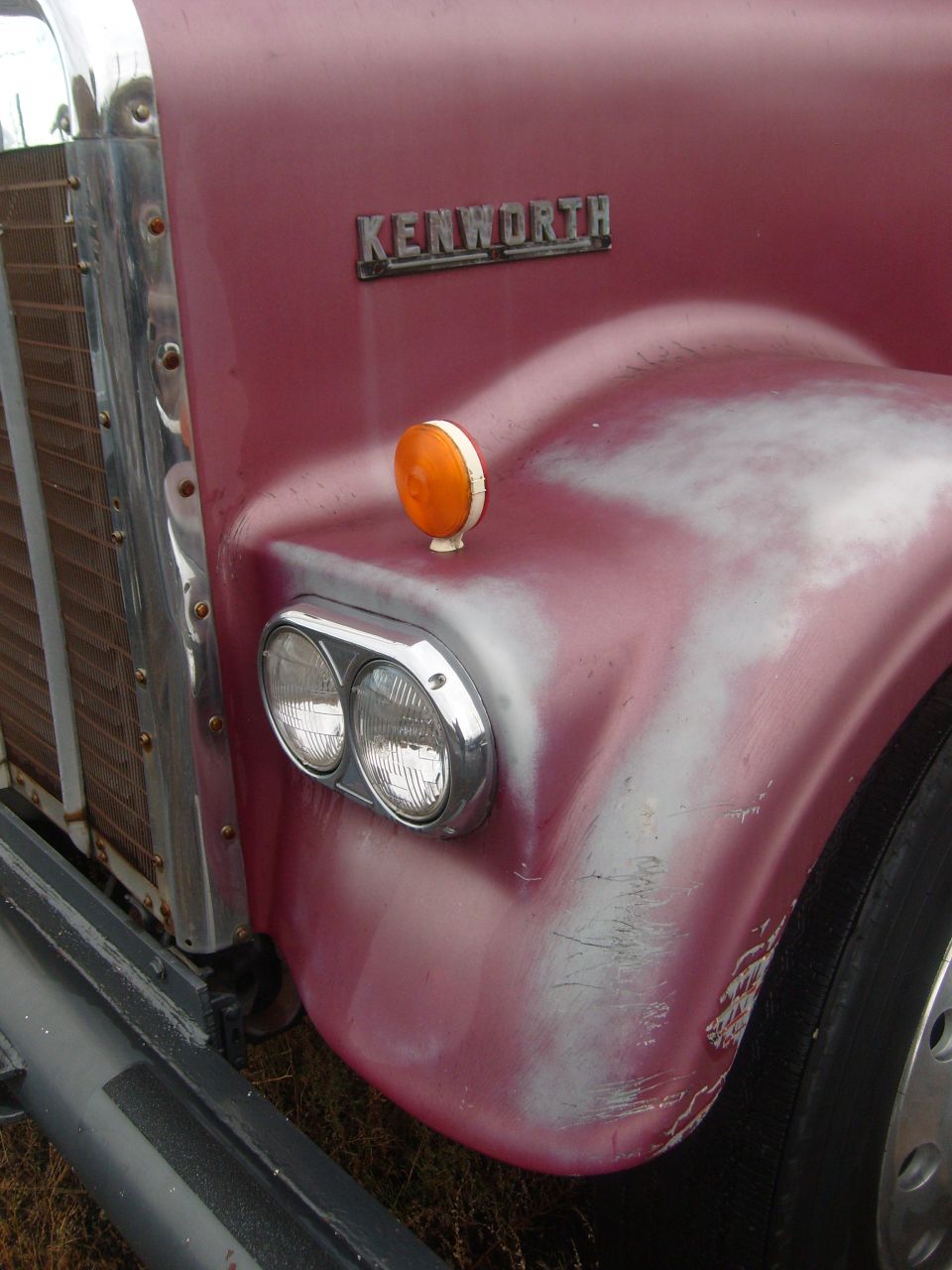 Chrome KENWORTH emblem and dual headlights on faded maroon truck fender