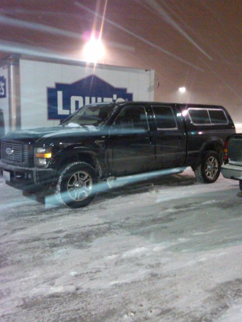 1988 Ford Bronco - A black Ford pickup truck with a camper shell is parked in a snowy lot, with a Lowe's delivery truck visible behind it.