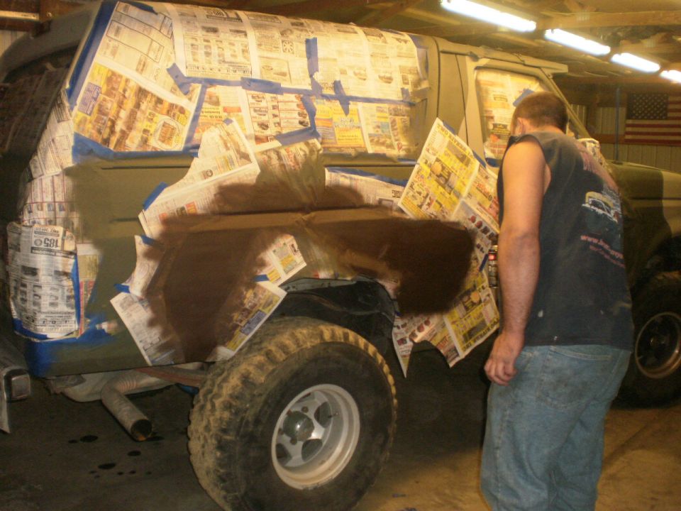 Man spraying brown camo pattern on a green truck quarter panel over newspaper masking