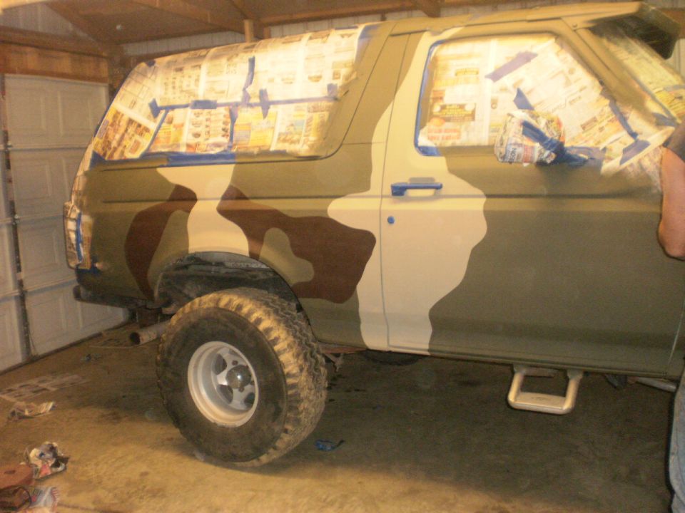 Two-door SUV being spray-painted camouflage with newspaper-masked windows