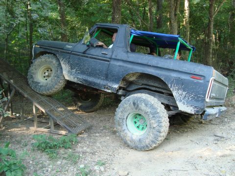 1979 Ford Bronco - This modified truck is attempting to climb a ramp in a wooded area, its off-road capabilities.