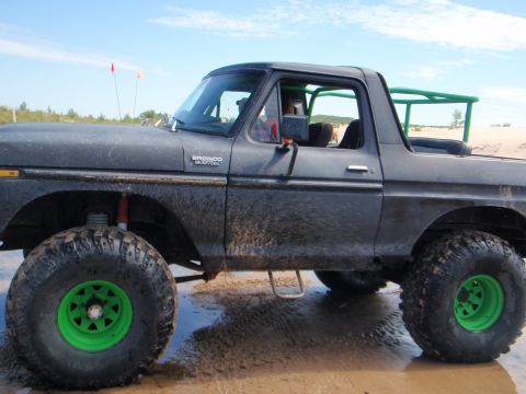 1979 Ford Bronco - This modified Ford Bronco is shown on a beach with a roll cage and bright green wheels.