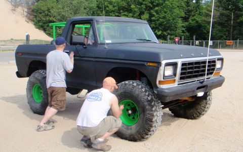 1979 Ford Bronco - A modified 1979 Ford Bronco is being worked on by two men, showing its off-road tires and custom roll cage.