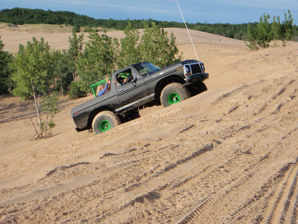 1979 Ford Bronco with green roll cage and bright green wheels climbing a sand dune