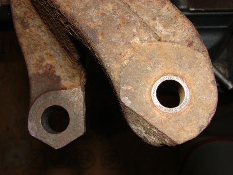 1993 Jeep Wrangler - Close-up comparing two rusty steel suspension control-arm links side by side, one bore fitted with a fresh metal bushing sleeve.
