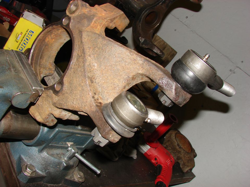 Rusted suspension parts, including ball joints and a spindle, held in a vise