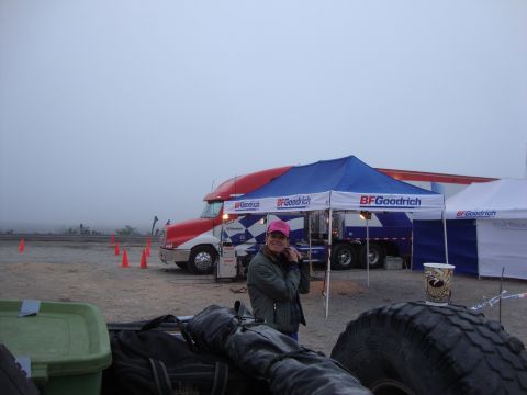 1990 Ford Bronco - person in a pink cap stands in front of a BFGoodrich semi-truck and branded tents in a foggy desert pit area.