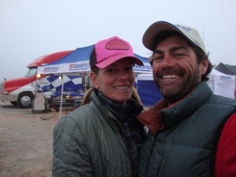 1990 Ford Bronco - smiling man and woman in caps pose together in front of a BFGoodrich semi-truck and branded tents in foggy conditions.