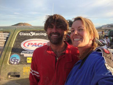 1990 Ford Bronco - smiling man in a red suit and a woman in blue pose closely beside a green race vehicle bearing PACE and Class 3 Racing decals at dusk.