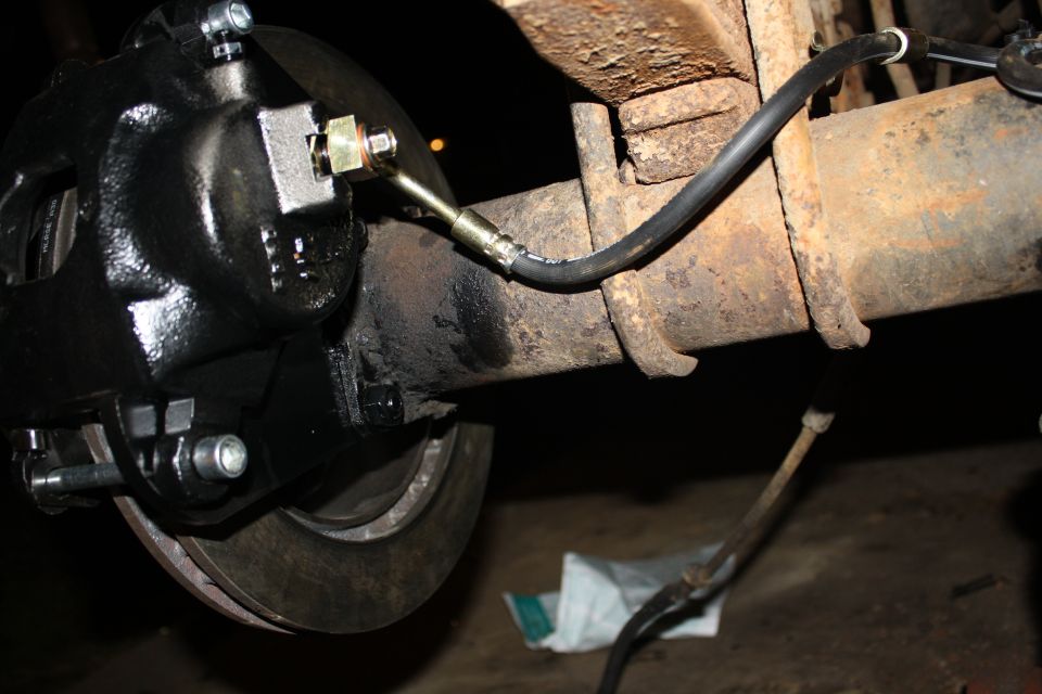 Close-up of a black brake caliper attached to a rusty axle with a brake line