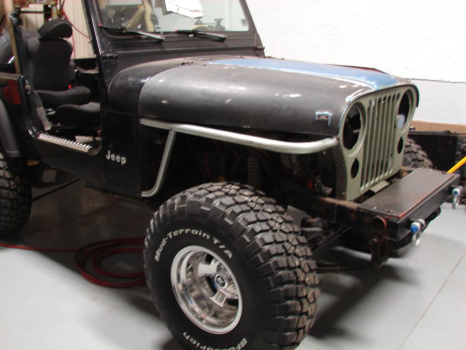 Black Jeep CJ-series with a green grille and aftermarket bumper, viewed from the front three-quarter angle
