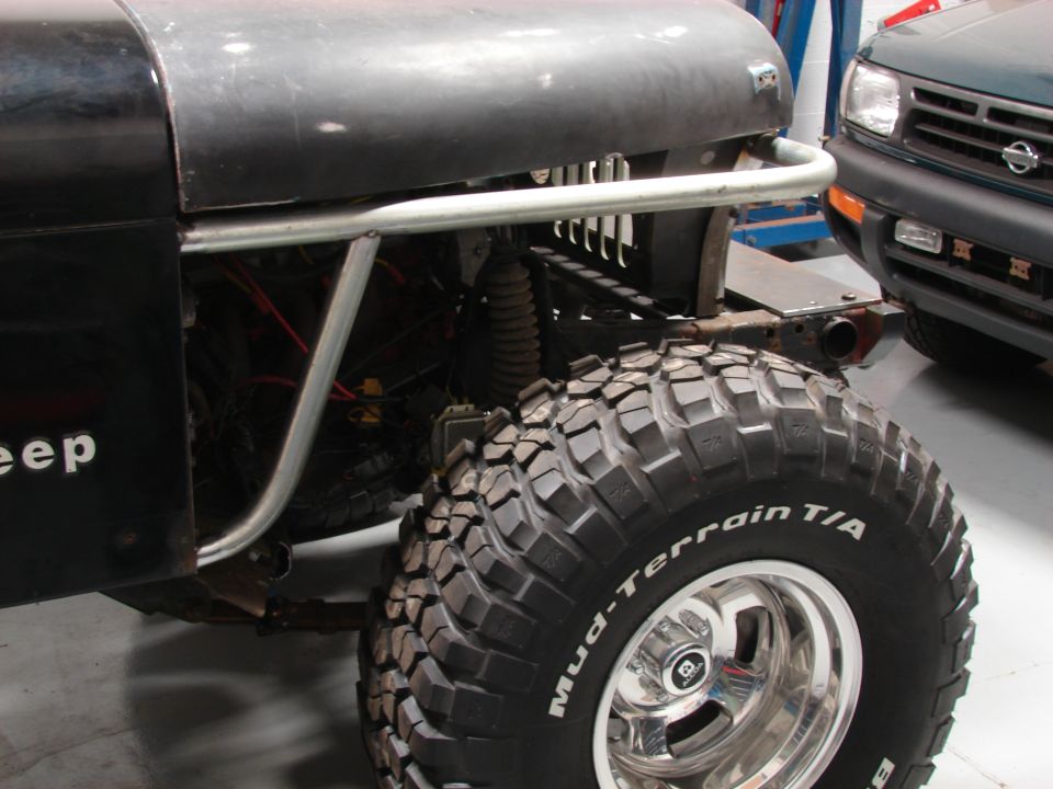 Jeep fender with "eep" visible, large Mud-Terrain T/A tire on chrome rim, and part of a green SUV in background