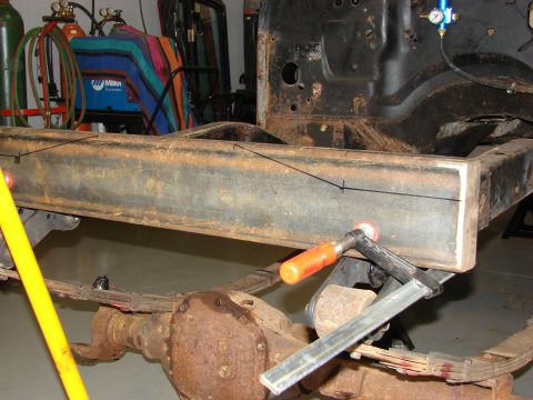 1993 Jeep Wrangler - A close-up view of a heavily rusted vehicle frame section, secured with a clamp and marked for modification.