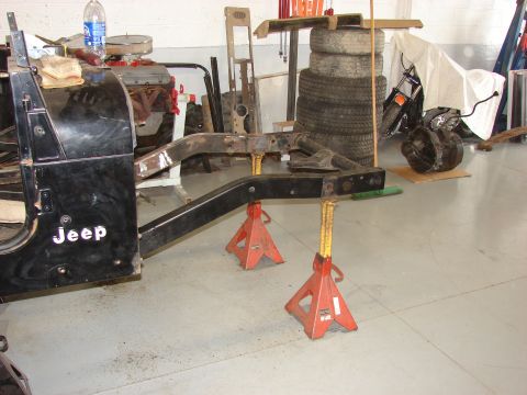 1993 Jeep Wrangler - The body and frame of a Jeep CJ-7 are elevated on jack stands in a garage, with other vehicle parts visible.