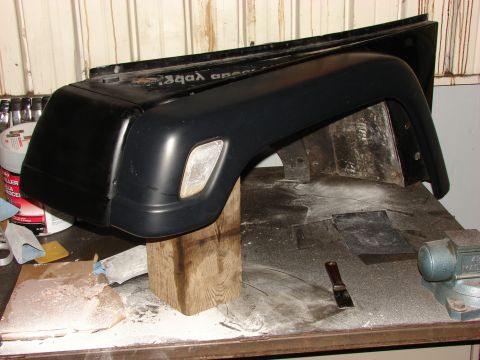 1993 Jeep Wrangler - A black Jeep fender and bumper assembly is shown on a workbench, possibly undergoing repair or modification.