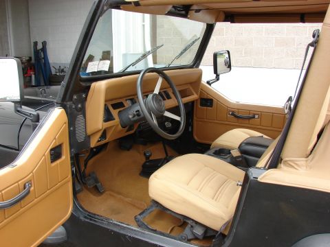 1993 Jeep Wrangler - The tan interior of a Jeep features bucket seats, a center console, and a dashboard with a steering wheel.