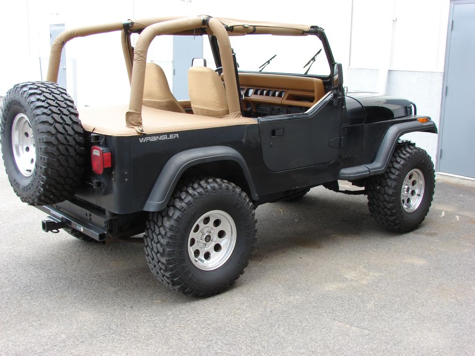 Black 1993 Jeep YJ Wrangler with tan soft top and spare tire on rear bumper, viewed from rear-right