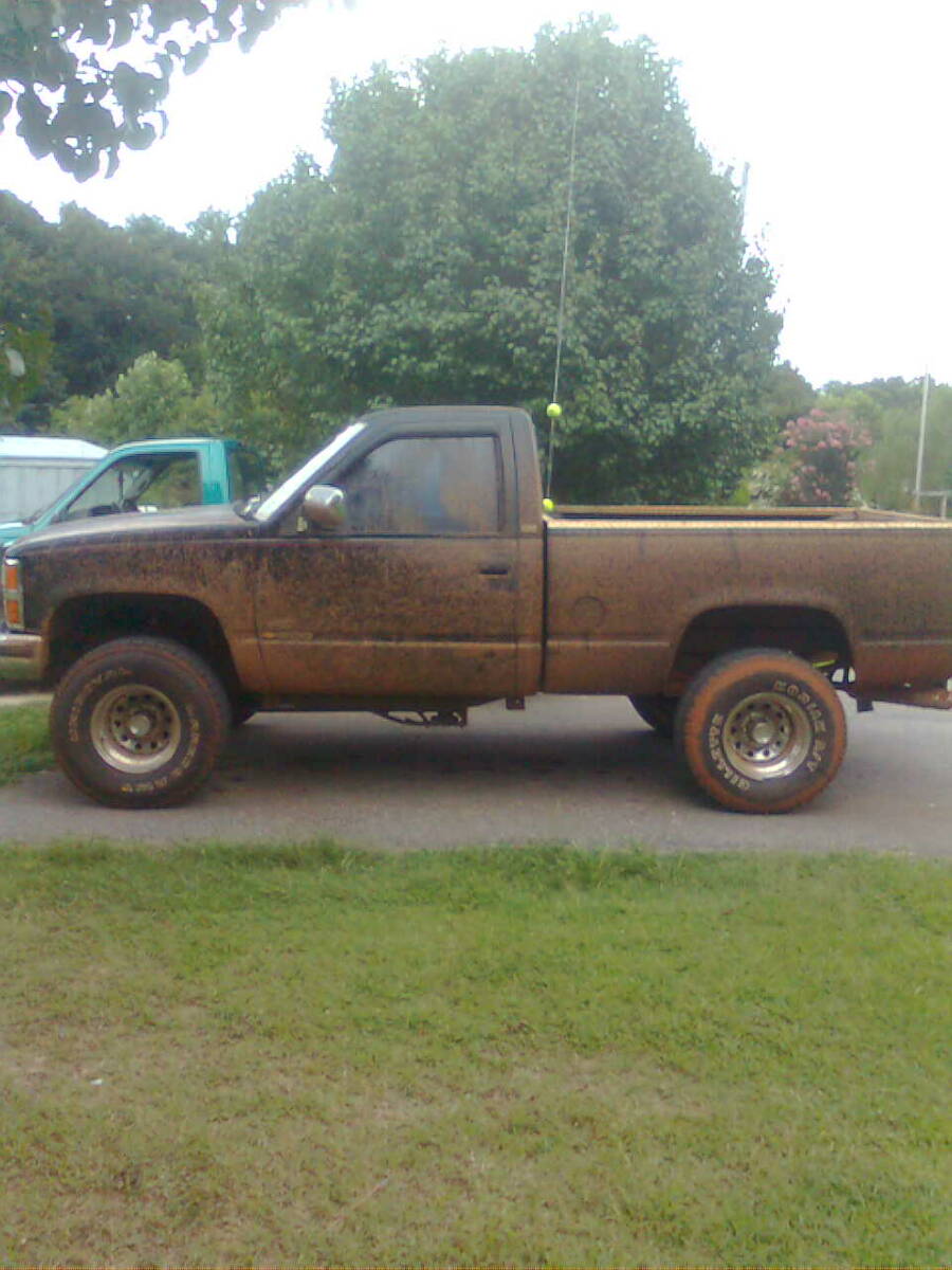 1991 Chevrolet C/K Pickup, side view, covered in mud. Another vehicle is partially visible to the left