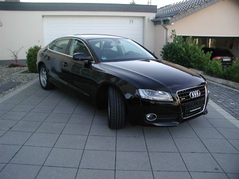 2010 Audi A4 - A black Audi A5 Sportback is parked in front of a garage, with another vehicle visible inside.