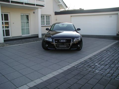 2010 Audi A4 - A black Audi is parked in a driveway in front of a house and garage. The license plate area has text.