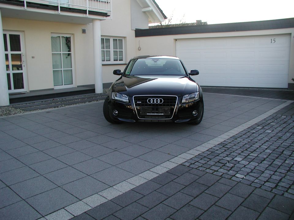 Black Audi parked in driveway in front of a garage. The grille has the Audi rings